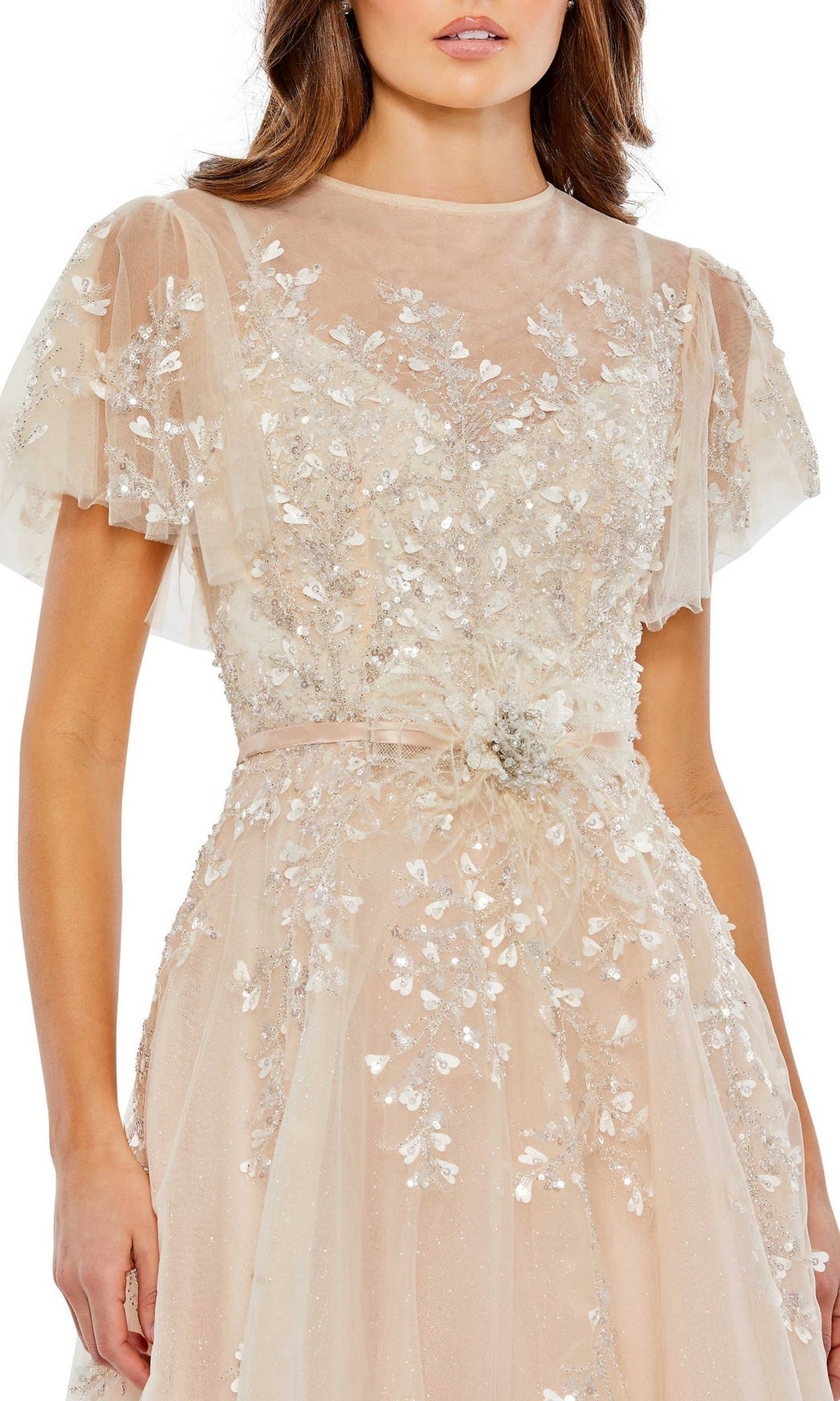 A woman wears the Long Formal Dress 20362 by Mac Duggal, a sheer beige tea-length A-line dress with silver floral embroidery, sequins, flutter sleeves, and a cinched waist.